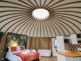 A round room with a bed dressed with orange pillows and a blanket a bathtub next to wooden paneled walls and a kitchen area with a sink and cabinets under a circular ceiling with wooden beams Lakeview Yurt Beckford near Tewkesbury