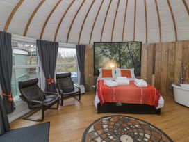 A bedroom with a bed with red bedding two black chairs windows with dark curtains and a bathtub against wooden walls at Lakeview Yurt in Beckford near Tewkesbury