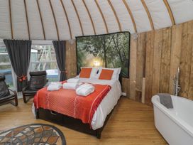 A bedroom with a double bed white and orange linens two black chairs wooden walls and a white bathtub with a towel at Lakeview Yurt in Beckford near Tewkesbury