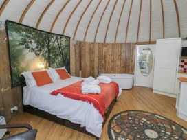 A bedroom with a double bed with orange pillows and blanket a bathtub a circular patterned rug and wooden walls at Lakeview Yurt Beckford near Tewkesbury
