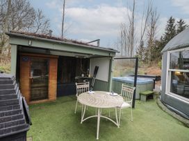 An outdoor area with a round table and two chairs a hot tub a small wooden sauna and a covered seating area at Lakeview Yurt Beckford near Tewkesbury