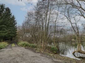 A gravel path next to a pond with trees and shrubs around at Lakeview Yurt Beckford near Tewkesbury