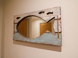 A mirror with a fish-shaped wooden frame in the hallway at Cliff Cottage