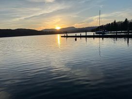 A scenic view of a lake at sunset with mountains and a boat at Tiggywinkle Beck - White Cross Bay Windermere