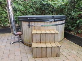 A hot tub with wooden steps on a brick patio at Caban Tan Y Dderwen in Chwilog