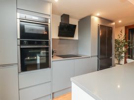 A kitchen with built-in oven, microwave, cooker hood, and refrigerator at Riverside Lodge Afonwen