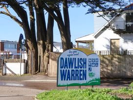 A sign for Dawlish Warren near trees and a building in Dawlish Warren