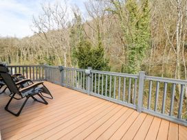 A deck with chairs overlooking trees at 33 Woodpecker Lodge in Llanarth