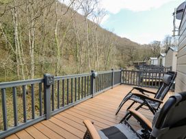 A deck with chairs overlooking a forested area at 33 Woodpecker Lodge Llanarth