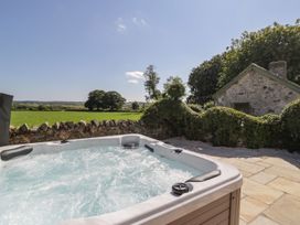 A hot tub next to a stone wall with a view of trees and fields at Ty Mawr Farm Llanfairpwllgwyngyll