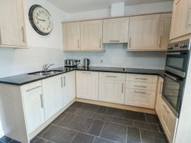 A kitchen with cabinets, sink, oven, and clock at Too Hoots in Lligwy