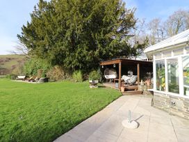 A garden with a pathway, deck, and hanging chair at Plas Dolguog in Machynlleth
