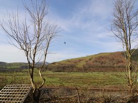 A landscape with trees and a plane flying over hills at Plas Dolguog in Machynlleth