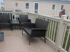 A deck with rattan furniture and a side table at Lynsey's Coastfields Caravan in Skegness