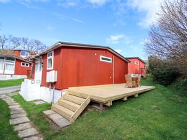 A red cabin with wooden deck and outdoor seating at Chalet 23 Erw Porthor Tywyn