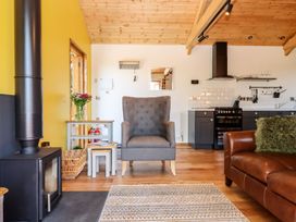 A living room with a stove, armchair, and kitchen elements at Nelli Lodge at Mile End, Crediton