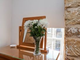 A flower vase on a wooden dresser with a mirror at Holly Cottage in Whitby
