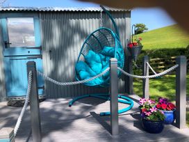 An outdoor seating area with a hanging chair and flower pots at The Peacock Shepherds Hut at Hafoty Boeth in Corwen
