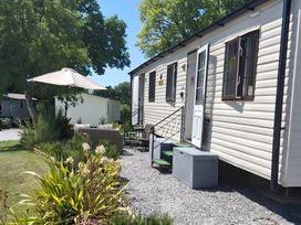 An outdoor area with a caravan, chairs, and an umbrella at Llanarmon-yn-Ial Mold 3-Bed Caravan, Sleeps 6 Llanarmon-Yn-Ial