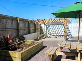 A garden with a wooden table and benches at Rhiwlas in Rhosneigr