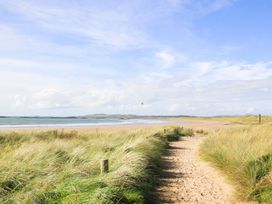 A beach with a sandy path and grass near the water at Rhiwlas in Rhosneigr
