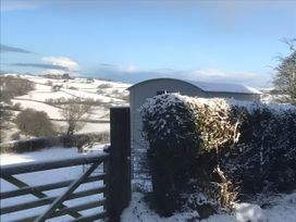 A snowy landscape with a fence and building at The Shepherds Hut at Hafoty Boeth Corwen