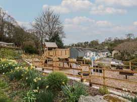 A playground with a playhouse and swings at Oak Cottage in Falmouth