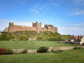 A castle with grassy area and houses in the foreground at Northrawe Bamburgh