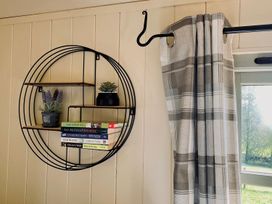 A shelf with books and plants next to a curtain and window at Cwt Tyddyn Shepherd's Hut in Corwen