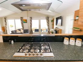 A kitchen with a gas stove and open living area at Wernlas Lodge in Oxwich