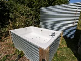 A hot tub with faucets surrounded by corrugated metal in the garden at Hares Hideaway Shepherd's Hut South Molton