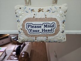 A sign reading 'Please Mind Your Head' with floral embroidery at Bobbin Nook in Staveley