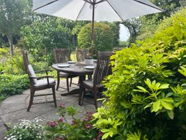 A garden with a wooden table and chairs under an umbrella at Cutbush Farmhouse in Norwich