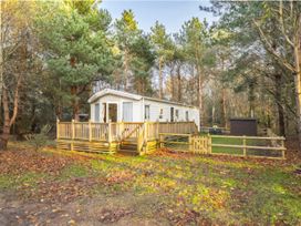A mobile home with a wooden deck and trees at Sprindrift - Kelling Heath Holiday Park in Holt