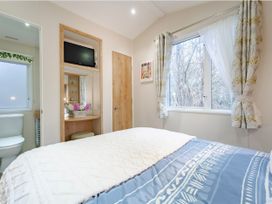 A bedroom with a bed, television, and a window at Sprindrift - Kelling Heath Holiday Park, Holt