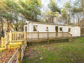 A cabin with decking and steps surrounded by trees at Sprindrift - Kelling Heath Holiday Park in Holt