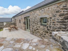 An outdoor area with a stone wall and wooden table at Dairy Cottage in Oxwich
