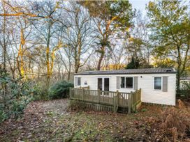 A cabin with a deck surrounded by trees at Prima -Kelling Heath Holiday Park in Holt