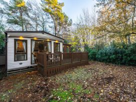 A cabin with a deck in a forested area at The But n Ben - -Kelling Heath Holiday Park Holt