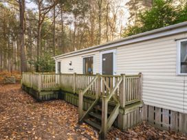 A mobile home with a deck surrounded by trees at Rawsons Retreat - Kelling Heath Holiday Park, Holt