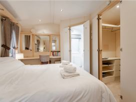 A bedroom with a bed, dresser, chair, and wardrobe at Rawsons Retreat - Kelling Heath Holiday Park in Holt