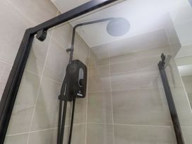 A shower with glass panel and showerhead at Y Byngalo Trearddur Bay