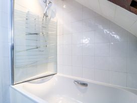 A bathtub with a shower and tiles at The Coach House Near Charminster