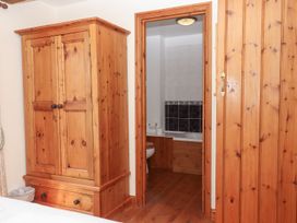 A bedroom with a wooden wardrobe and an adjoining bathroom with a toilet and bathtub at The Cottage in Sampford Courtenay