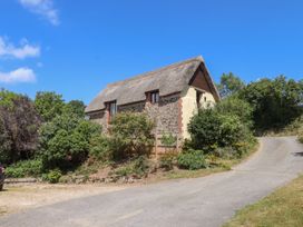 A thatched cottage with a stone wall and surrounding greenery at The Cottage in Sampford Courtenay