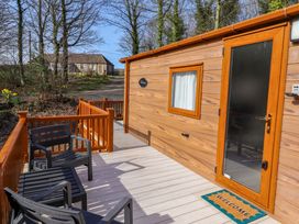 A wooden cabin with a welcome mat and outdoor seating in front at Gardeners Lodge 