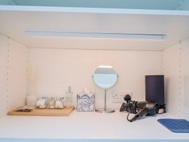 A bathroom shelf with a hair dryer and perfume bottle at Le Petit Glen in Uplyme