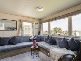 A living room with a sectional sofa and windows at Estuary View in Allhallows
