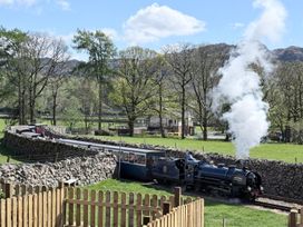 A steam train on a track with a stone wall and trees at Pandora in Holmrook