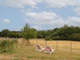A view of two deck chairs on grass with trees and a field at The Byre in Conwy